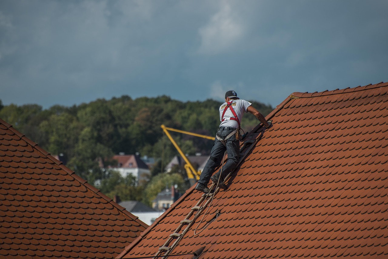 Roofer in a safety harness on a tiled roof under a stormy sky