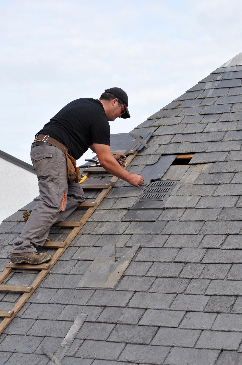 Roofer on a ladder replacing slates on a grey slate roof